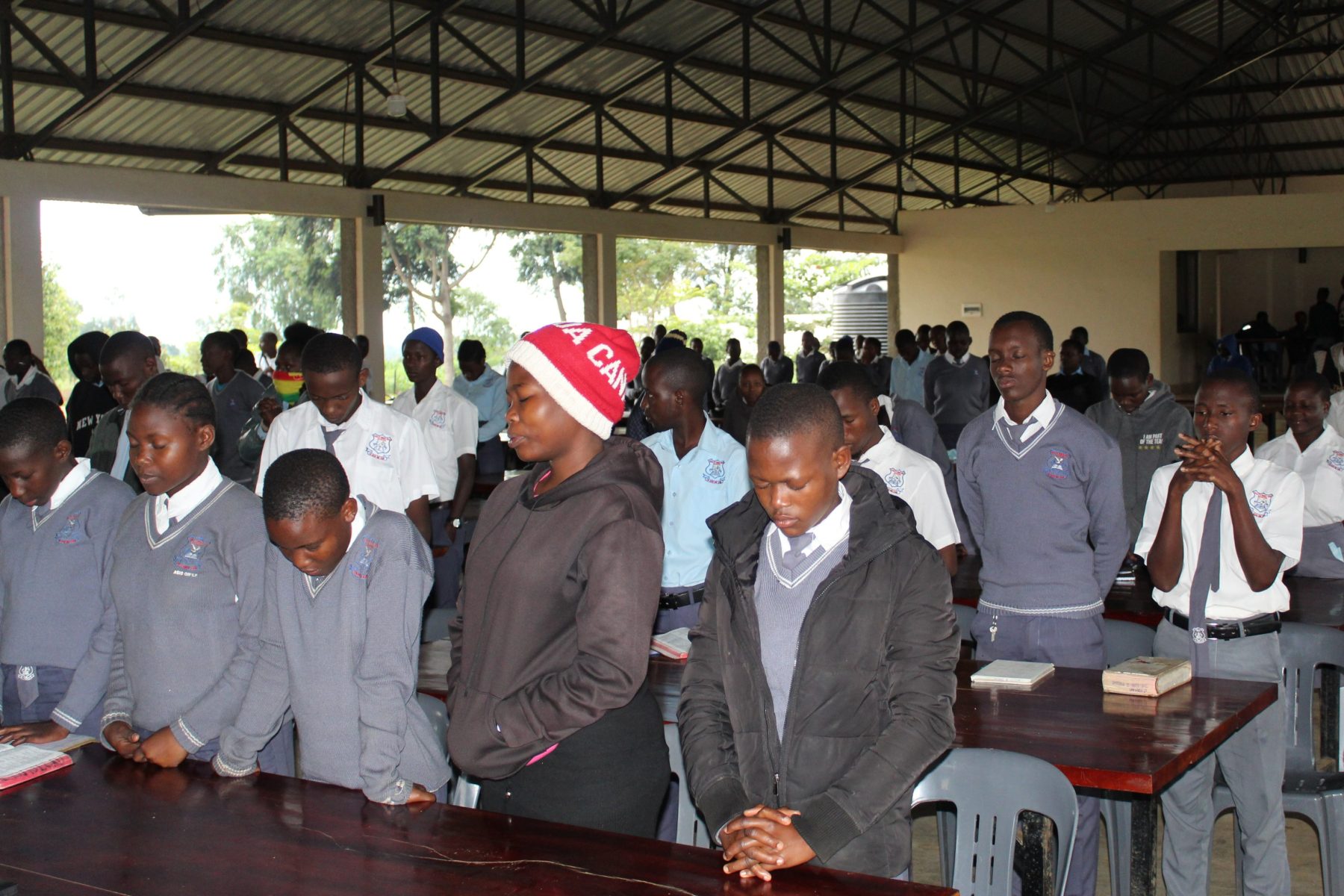 In this photo, a large number of high school students are standing and praying during a chapel service.