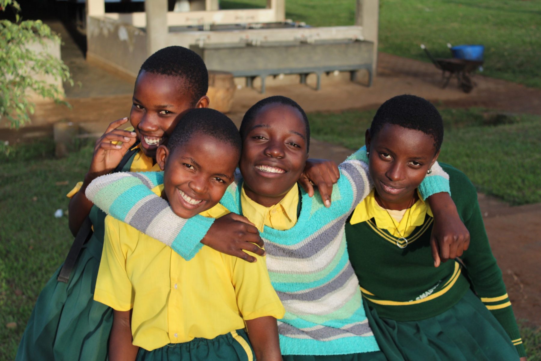 Four Primary School student are standing close together, smiling happily.
